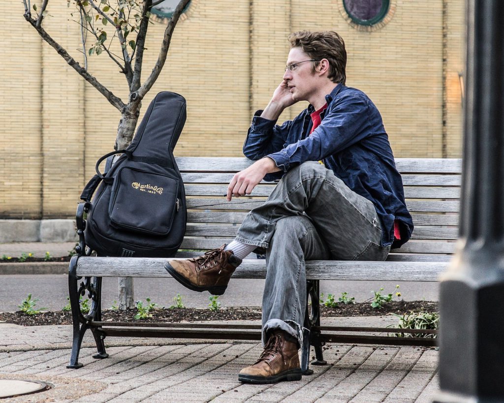 男性がベンチに座りギターケースの横で電話している画像