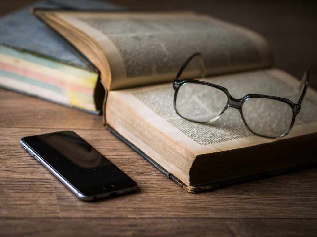 机の上に本とメガネ、スマートフォンが置いてある画像